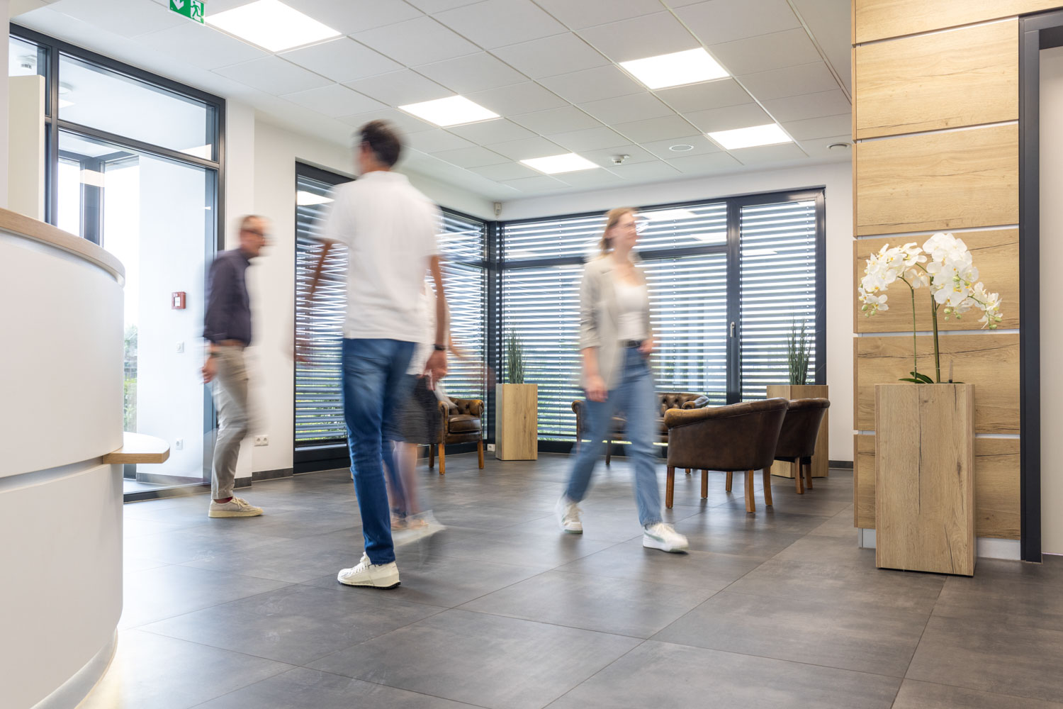 Moderner Büroempfang mit Menschen in Bewegung, helle Räume, offene Arbeitsumgebung, Unternehmensarchitektur.